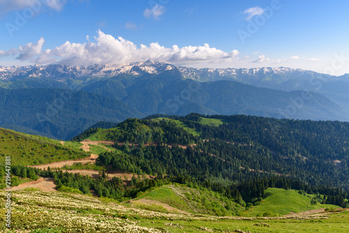 Beautiful view of the mountain range of the Caucasian mountains from the top of the Rosa Peak, Sochi, Russia. Mountain road serpentine going through the forest