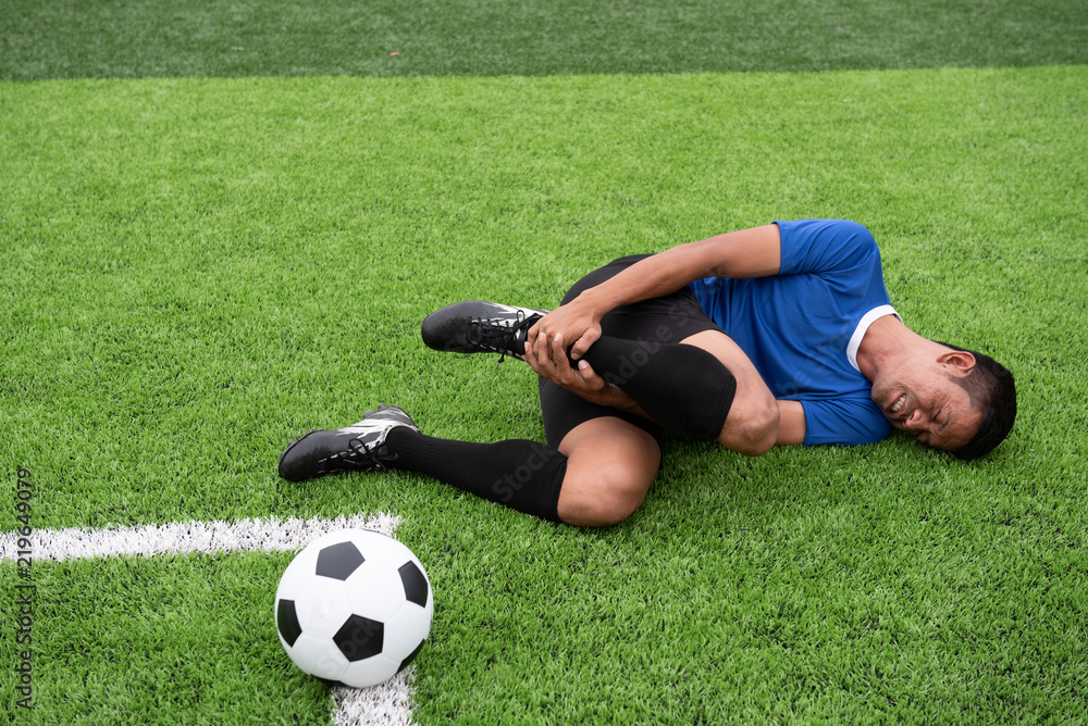 Fototapeta premium Footballer wearing a blue shirt, black pants injured in the lawn during the race.
