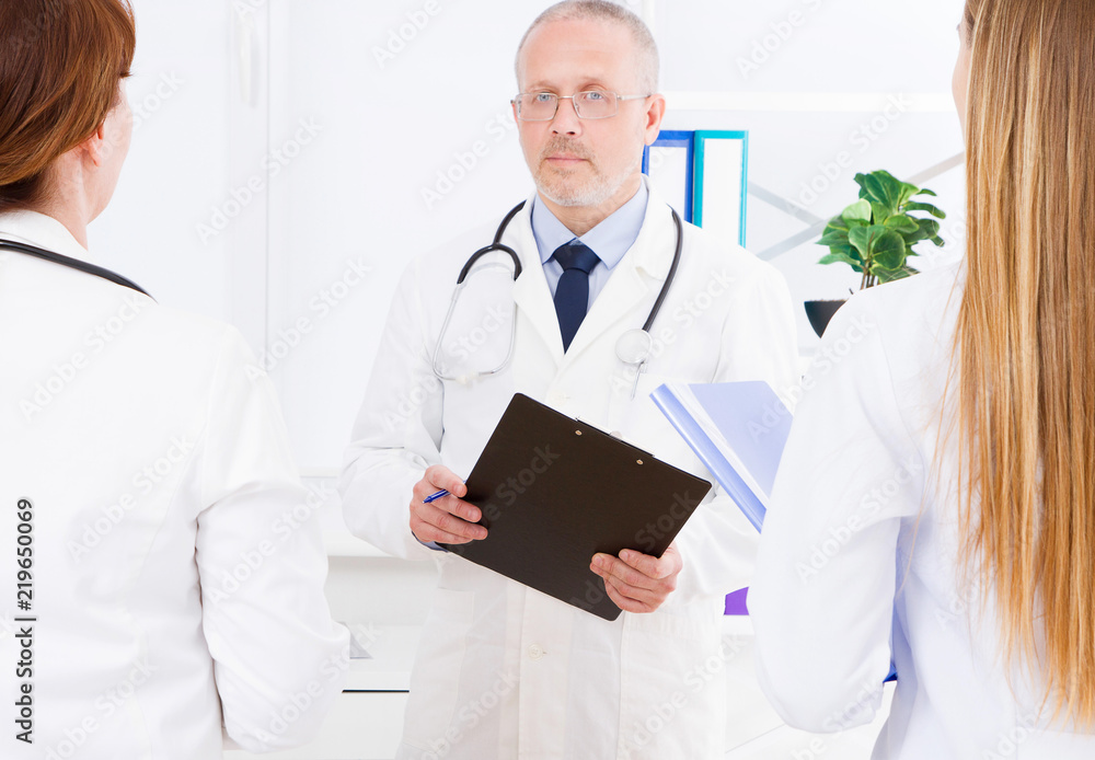 doctor posing in office with medical staff, he is wearing a stethoscope. Quality medicine concept. Man in white uniform. Medical insurance. Selective focus. Copy space doctor posing in office with medical staff, he is wearing a stethoscope. Quality medicine concept. Man in white uniform. Medical insurance. Selective focus. Copy space