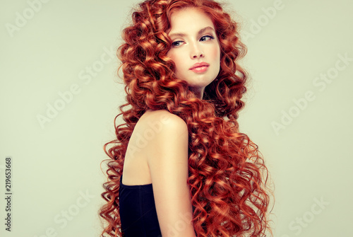Beautiful model girl with long red curly hair .Red head . Care and beauty hair products 
