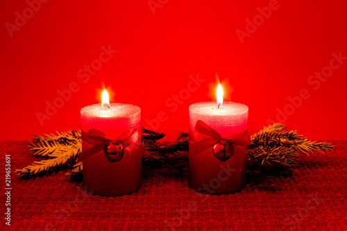 Two red candles and green spruce branches against a red background in Finland.