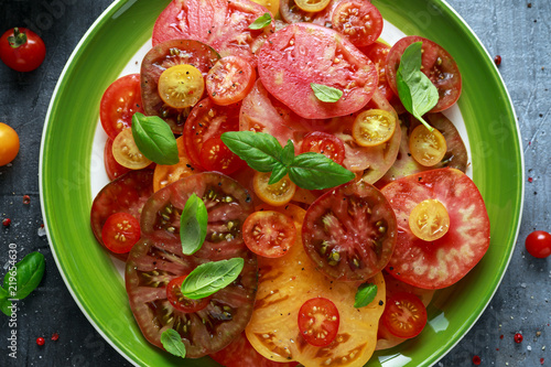 Colorful Tomato Salad with heirloom, pear shaped, beef heart, tigerella, brandywine, cherry, black tomatoes in a green plate. healthy food photo