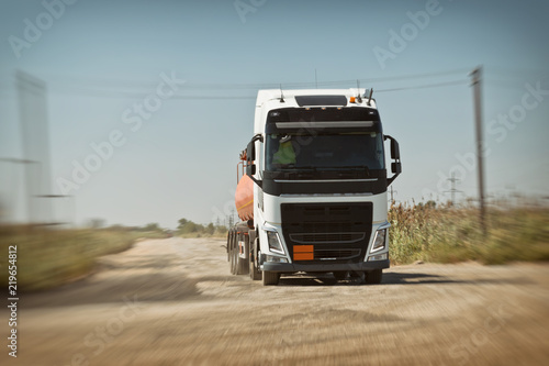 A truck with an orange tank goes on a knurled unpaved road