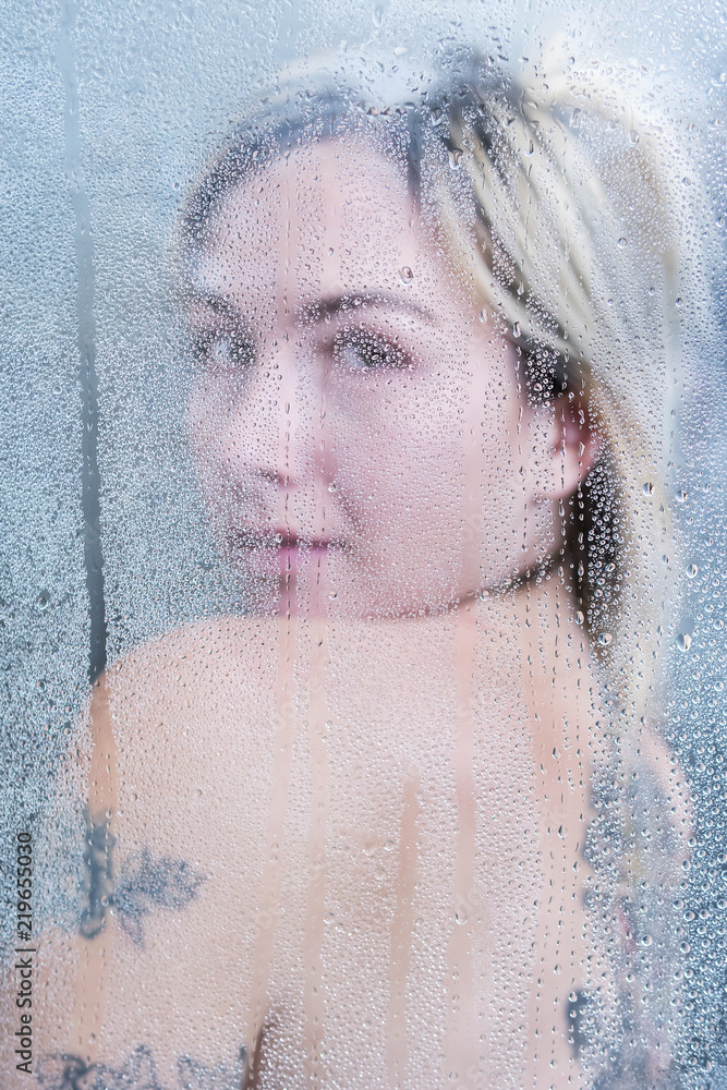 Beautiful woman with a tattoo in the shower turned around, showing her shoulder