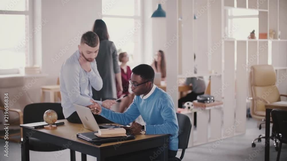 Two casual multiethnic colleagues collaborate in modern healthy workplace, Caucasian confident female boss walking by. Two casual multiethnic colleagues collaborate in modern healthy workplace, Caucasian confident female boss walking by.