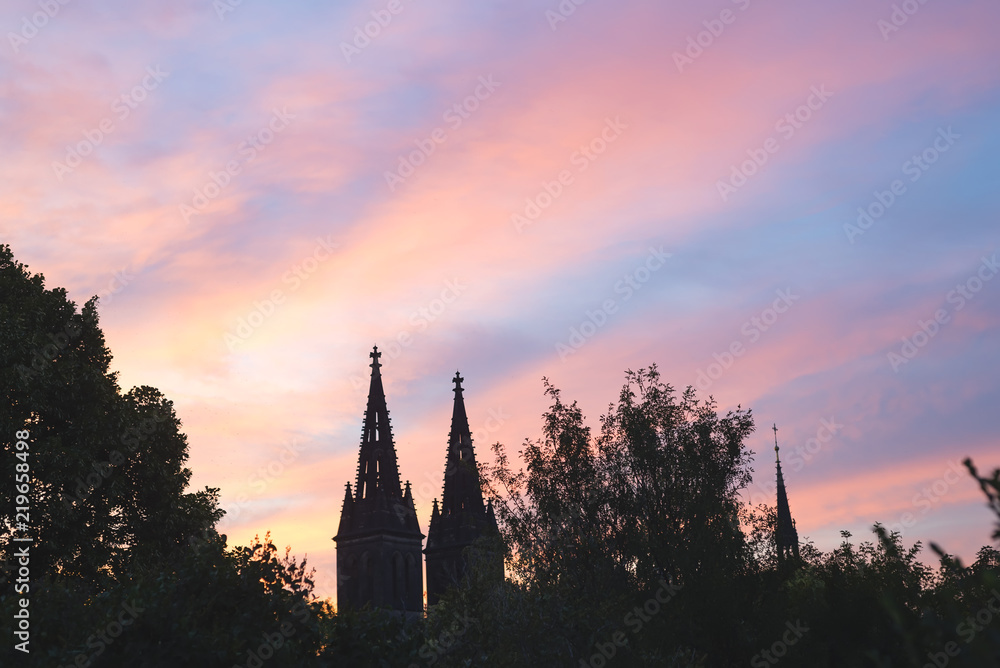 Obraz premium towers Church of St Ludmila Kostel sv. Ludmily in Prague in the distance against the background of the sunset and the pink sky and green forest