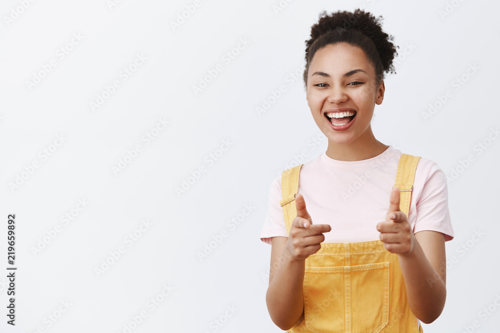 Hey I know you. Portrait of friendly-looking optimistic and kind african-american teenage girl in trendy yellow overalls, pointing at camera with fingergun gesture and smiling broadly Hey I know you. Portrait of friendly-looking optimistic and kind african-american teenage girl in trendy yellow overalls, pointing at camera with fingergun gesture and smiling broadly