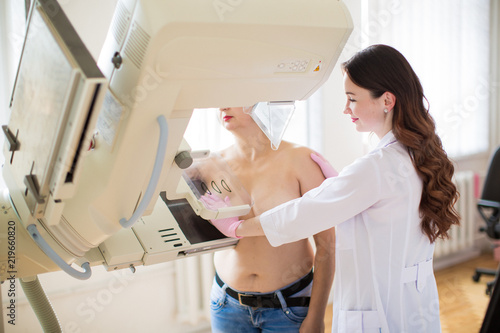 Side view of the young happy breast specialist who is carrying out the ultrasound examination of the breast of a patient in her office