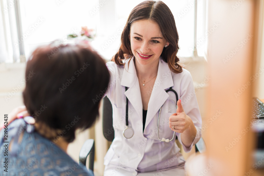 The young cheerful breast specialist talking with the patient in her office and showing thumb up The young cheerful breast specialist talking with the patient in her office and showing thumb up
