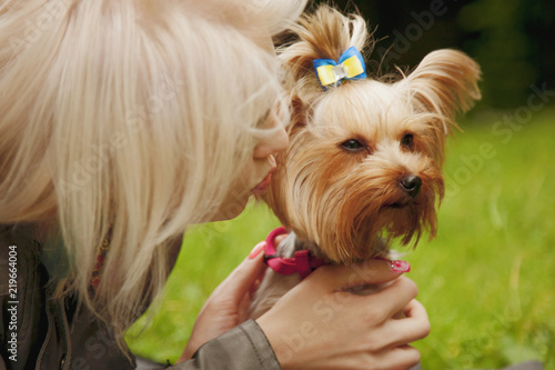 Cute small dog in the arms of a beautiful young girl licking her face outdoors