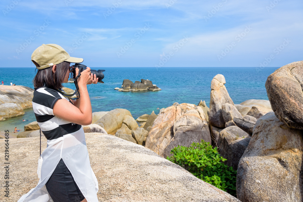 Young woman are using a DSLR camera to photography of the Hin Ta Hin Yai and beautiful nature landscape of blue sea and sky during summer travel at Koh Samui island, Surat Thani, Thailan