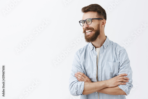 Creative happy and funny bearded man with moustache in glasses with black rim turning left laughing out loud enjoying interesting and hilarious conversation holding hands crossed on chest relaxed