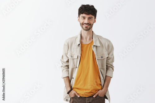 Good-looking creative and stylish hipser european male with beard in trendy outfit holding hands in pockets walking down street and enjoying chilly summer evening feeling happy and satisfied