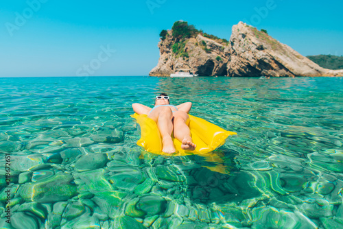 woman laying at yellow inflatable mattress in blue clear transparent sea water
