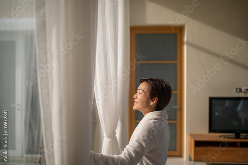 Asian woman standing at window and facing sunlight with her smiling face