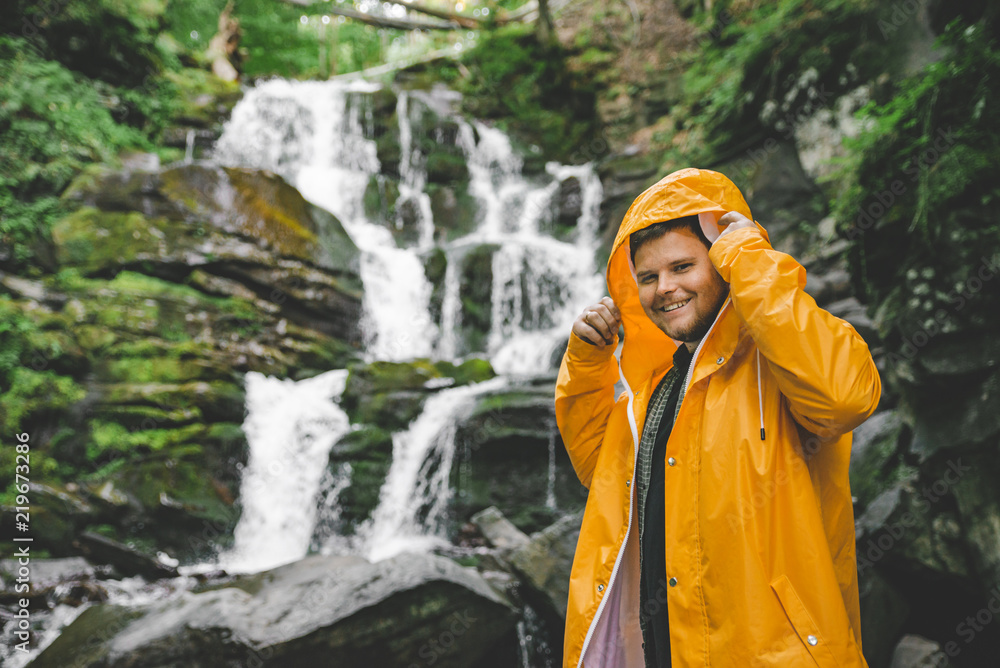 man standing in yellow raincoat and looking at waterfall