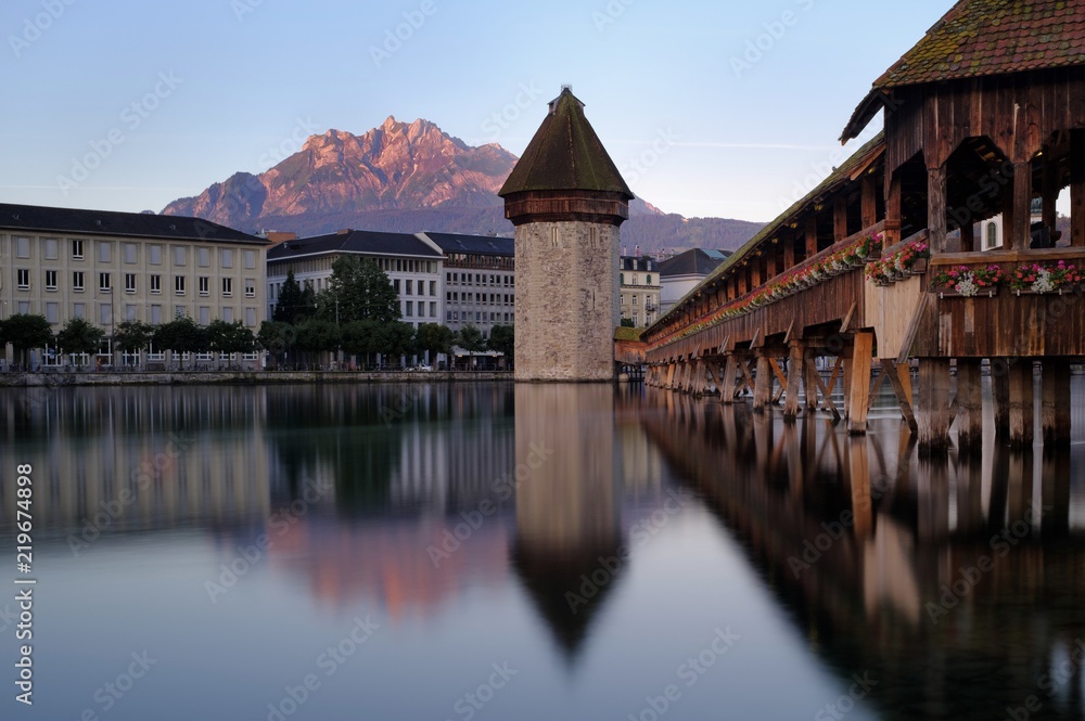 Fototapeta premium Die Kapellbrücke in Luzern. Im Hintergrund der Berg Pilatus im ersten Morgenlicht.