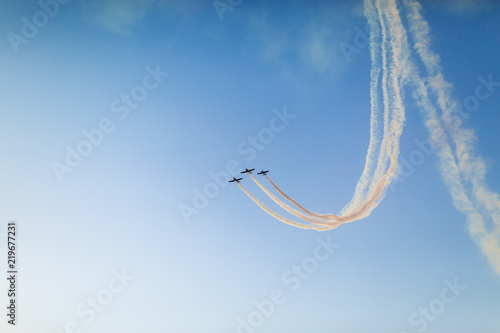 Unidentifiable airplanes performing acrobatic flight on blue sky. Trace of Smoke behind photo