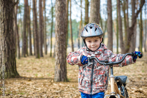 Happy kid boy of 3 or 5 years having fun in autumn forest with a bicycle on beautiful fall day. Active child wearing bike helmet. Safety, sports, leisure with kids concept.