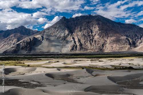 Sand Dune of Nubra Valley with mountains in background and cloudy blue sky in summer of Leh Ladakh, Jammu and Kashmir, India