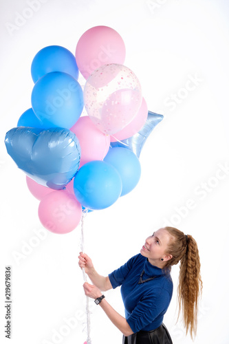 Attractive caucasian redhead girl in blue sweater smiling and holding in greetings manner pink and blue balloons, isolated