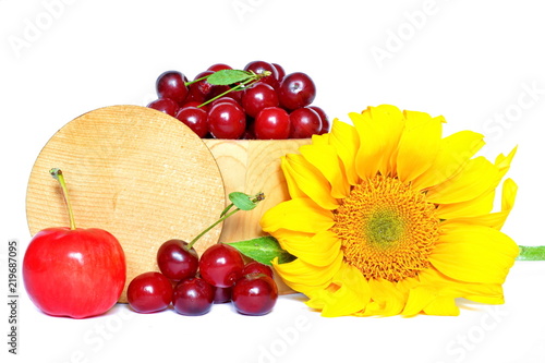 Fototapeta Naklejka Na Ścianę i Meble -  Rustic wooden barrel full of harvested red fresh raw sweet ripe cherry, juicy delicious apple next few berries and yellow flower of sunflower with round lid on white background. Isolated