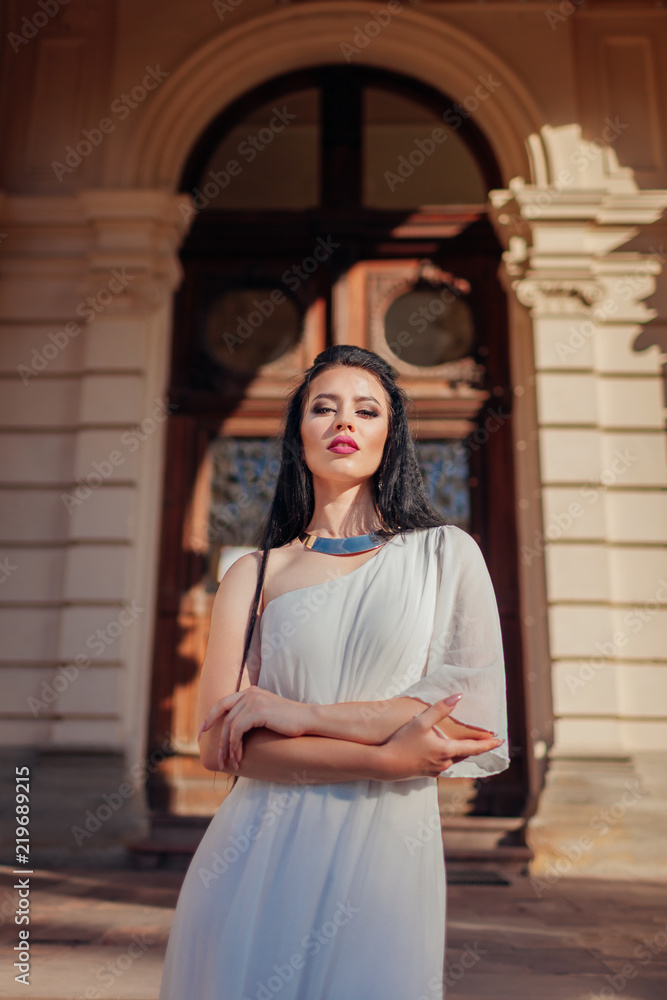 Fototapeta premium Beautiful woman wearing white wedding dress, accessories and jewellery on ancient architecture background outdoors.