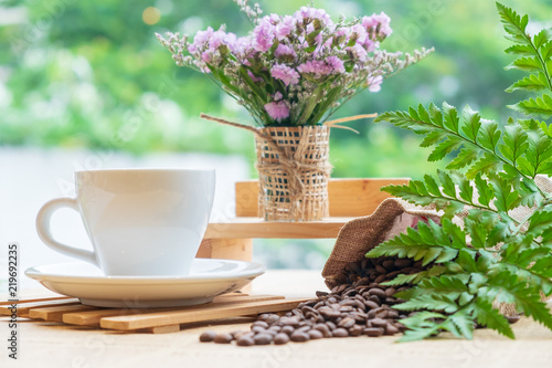 White cup of black coffee or tea on wooden plate over blurred coffee bean with nature sun lighting.