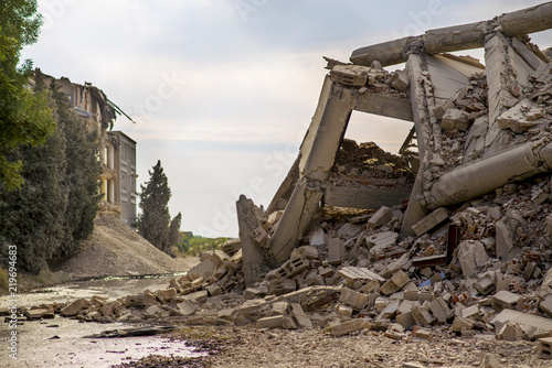 Industrial concrete building destructed by strike. Disaster scene full of debris, dust and crashed buildings with rising sun and blue sky