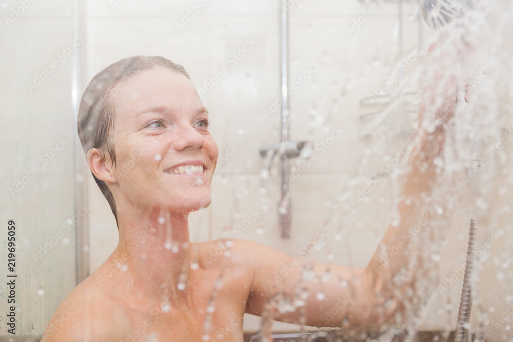 The young woman uses a shower in the bathroom of her house The young woman uses a shower in the bathroom of her house