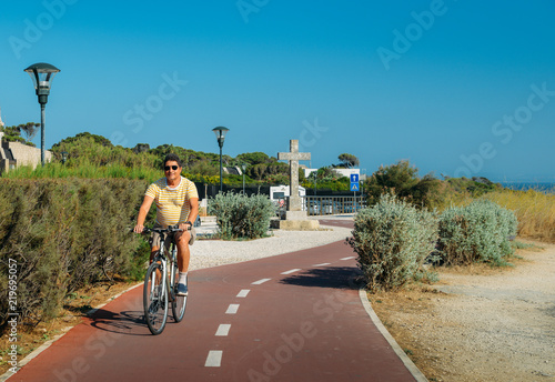 Mature man (55-60) cycles along a cycling path near Praia do Guincho and Roca do Cabo near Cascais, Portugal during a summer day