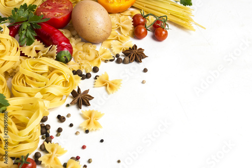 Italian pasta of different kinds with spices, red hot pepper, chicken eggs, yellow and red tomatoes on a white stone background. Concept cooking Italian pasta and sauce. Flat lay, top view