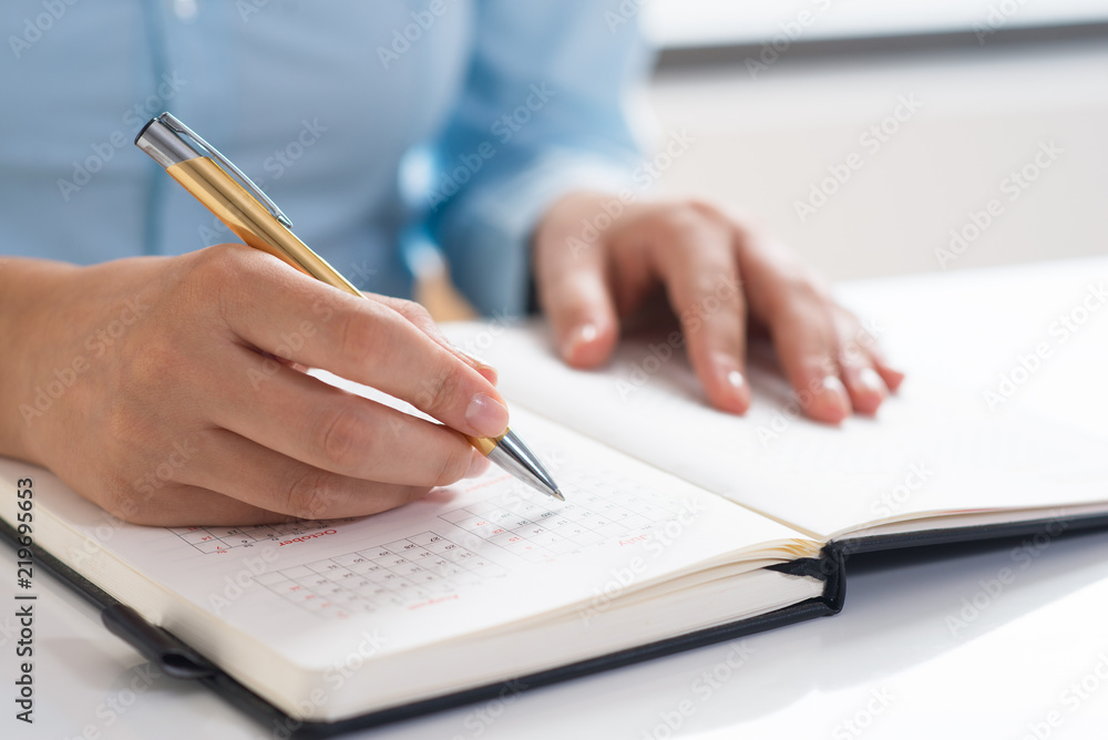 Closeup of woman using diary and scheduling. Entrepreneur sitting at desk. Planning concept. Cropped view. Closeup of woman using diary and scheduling. Entrepreneur sitting at desk. Planning concept. Cropped view.