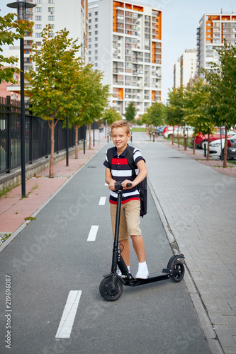School boy in riding with his electric scooter in the city with backpack on sunny day. Child in colorful clothes biking on way to school © glazunoff