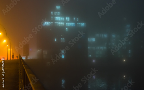Photography A woman walks at a foggy night over a bridge