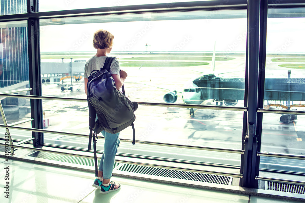 Travel tourist standing with luggage watching at airport window. Unrecognizable woman looking at lounge looking at airplanes while waiting at boarding gate before departure. Travel lifestyle. Travel tourist standing with luggage watching at airport window. Unrecognizable woman looking at lounge looking at airplanes while waiting at boarding gate before departure. Travel lifestyle.