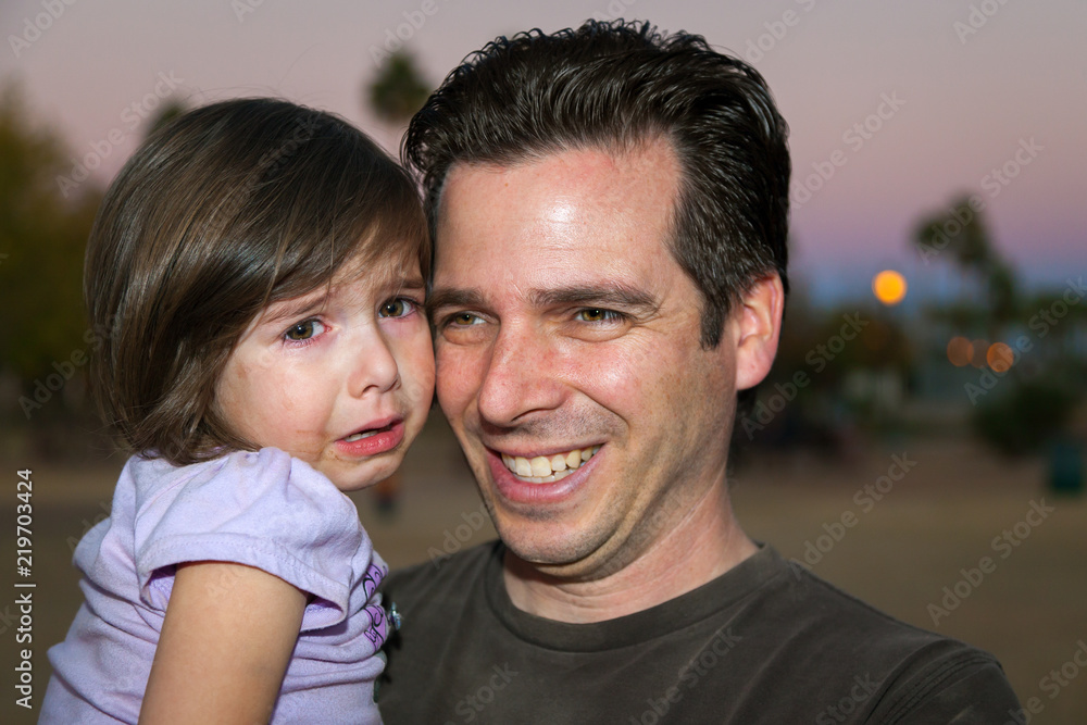 Father Holding His Crying Young Daughter She Has Tears and a Messy Food Face He is Smiling at Someone off Camera Father Holding His Crying Young Daughter She Has Tears and a Messy Food Face He is Smiling at Someone off Camera