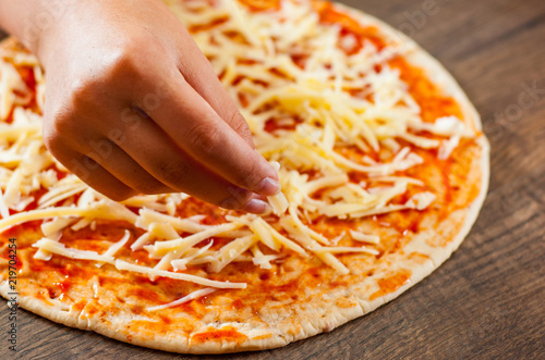 Cooking pizza. hand woman cook pouring grated cheese on dough. making Italian pizza on wooden background photo