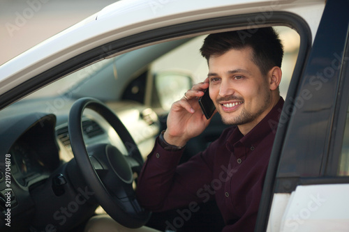 beautiful young guy in a shirt sitting in the car and talking on the phone