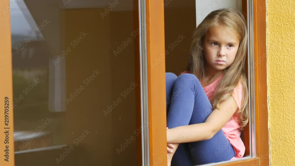 Sad young girl looking through a window at home Sad young girl looking through a window at home