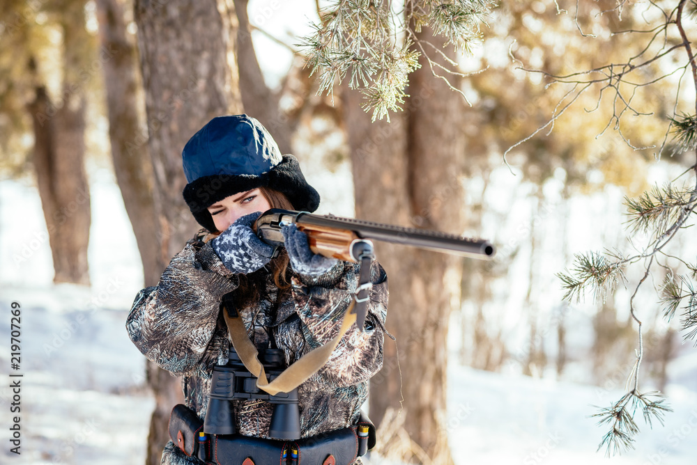 Naklejka premium A beautiful hunter in a camouflage suit walks through the woods with weapons, preparing to hunt.