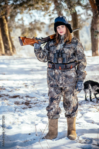 A beautiful hunter in a camouflage suit walks through the woods with weapons, preparing to hunt.