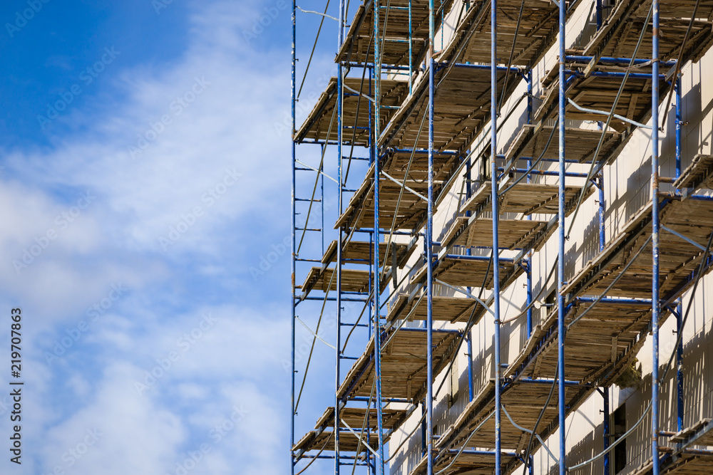 Scaffolding near a new house under construction as the temporary support building structure during construction against the blue sky.