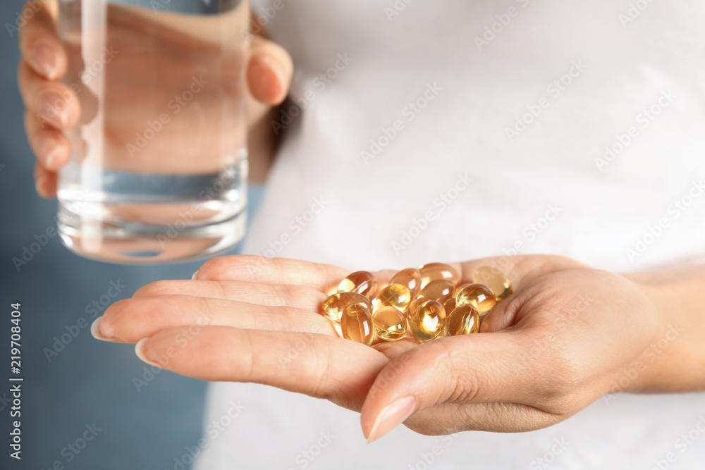 Woman with fish oil pills and glass of water, closeup Woman with fish oil pills and glass of water, closeup