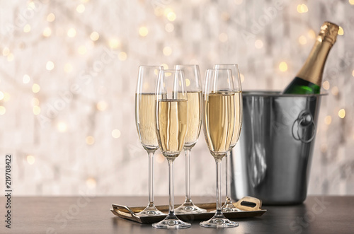 Glasses with champagne and bottle in bucket on table against blurred lights