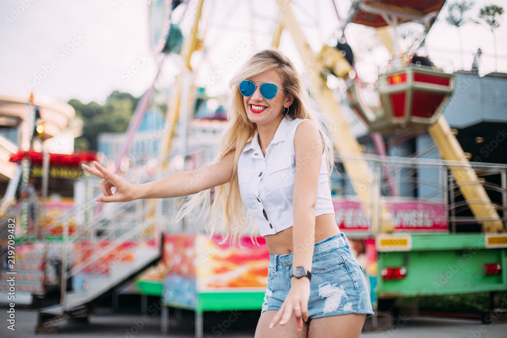 Stylish happy young woman wearing short denim shorts and a white T-shirt. brightred lips . portrait of smiling girl in sunglasses greet friends and laughter