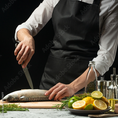 Preparation of mackerel by the chef, on a black background with lemons, limes