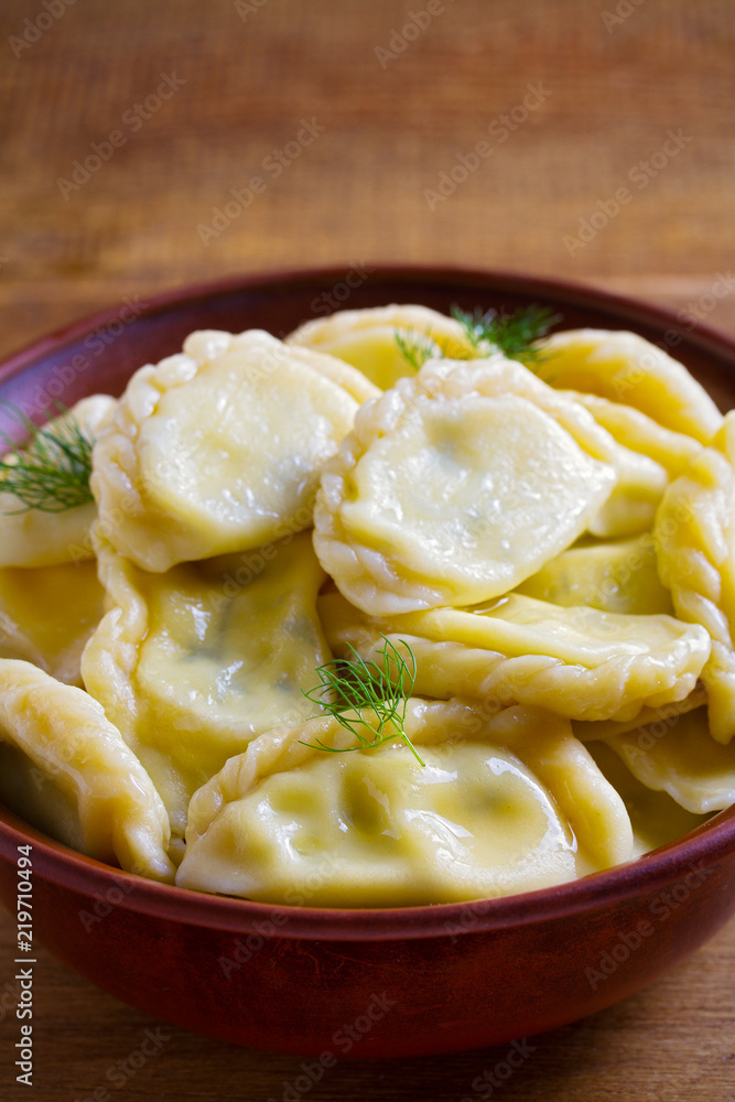 Dumplings, filled with cheese - vegetarian dish. Varenyky, vareniki, pierogi, pyrohy in a bowl on wooden table. vertical