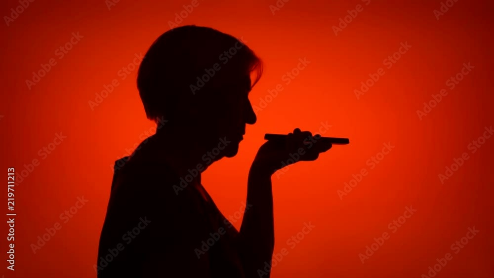 Silhouette of senior woman using mobile on red background. Female's face in profile talking on cellphone. Black contur shadow of grandmother's half-face Silhouette of senior woman using mobile on red background. Female's face in profile talking on cellphone. Black contur shadow of grandmother's half-face