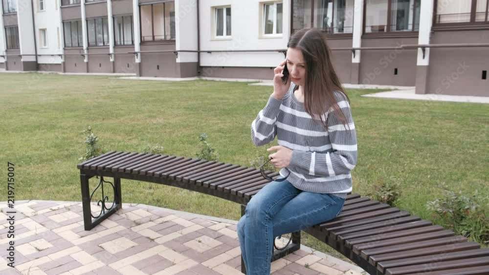 Woman is calling mobile phone sitting on the bench near the house. Woman is calling mobile phone sitting on the bench near the house.